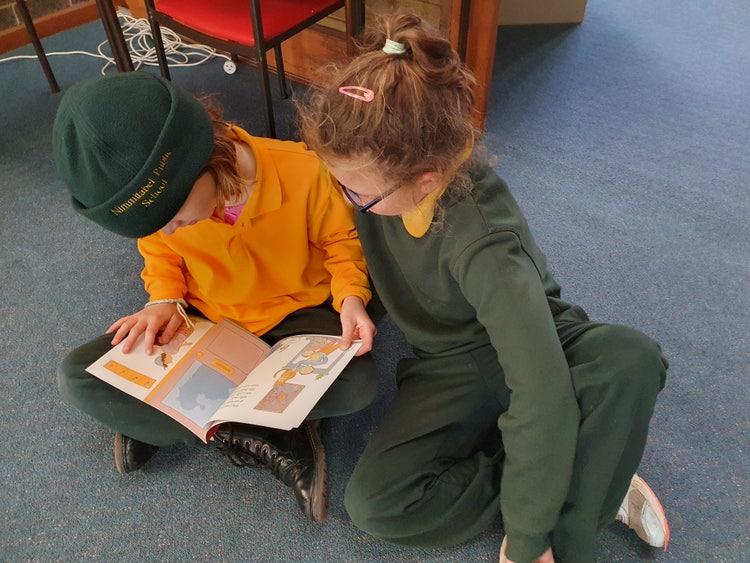 Two students sitting on the floor reading a book together