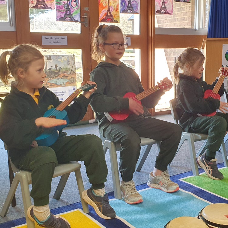 Three students playing ukuleles at a school assembly