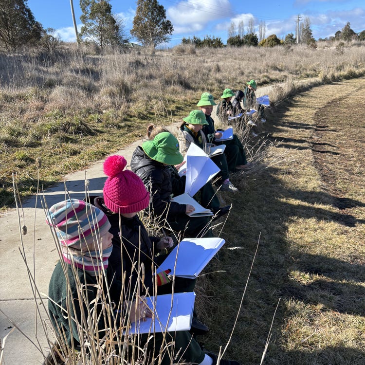 Students sitting along a walking path with sketchbooks.